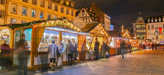 Strasbourg Christmas Market at night with festive lights, wooden stalls, and a large decorated Christmas tree, showcasing traditional French holiday charm.