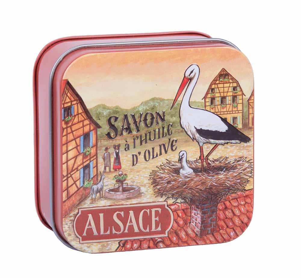 La Savonnerie de Nyons introduces its luxurious cotton flower soap, encased in the beautifully crafted 'La Cigogne' vintage tin. This tin, adorned with artwork by Luc Mazan, features the iconic stork of Alsace with her baby, perched atop a quaint village house, symbolizing happiness and prosperity.